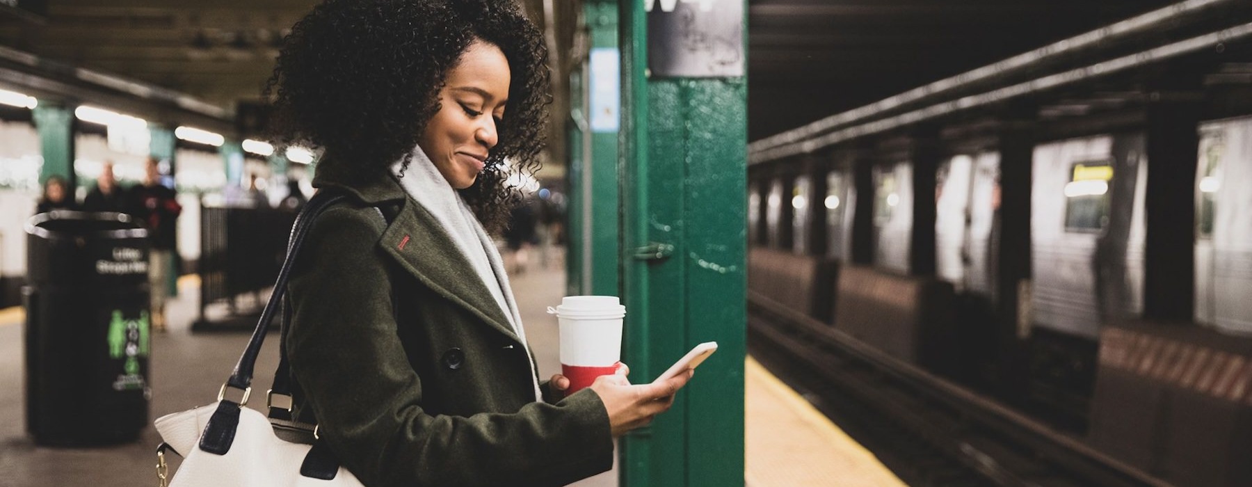woman with a cup of coffee texts on subway station platform